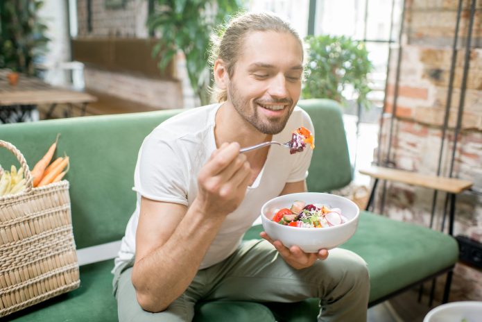Vegetarischer Mann isst Salat in einem Haus